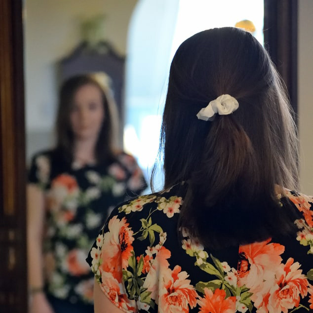 White woman wearing a black shirt with orange and green flowers looking in the mirror by Taylor Smith via Unsplash